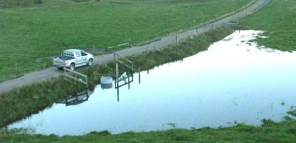 Aerial shot of paddock flooding blocked by a raised gravel road.