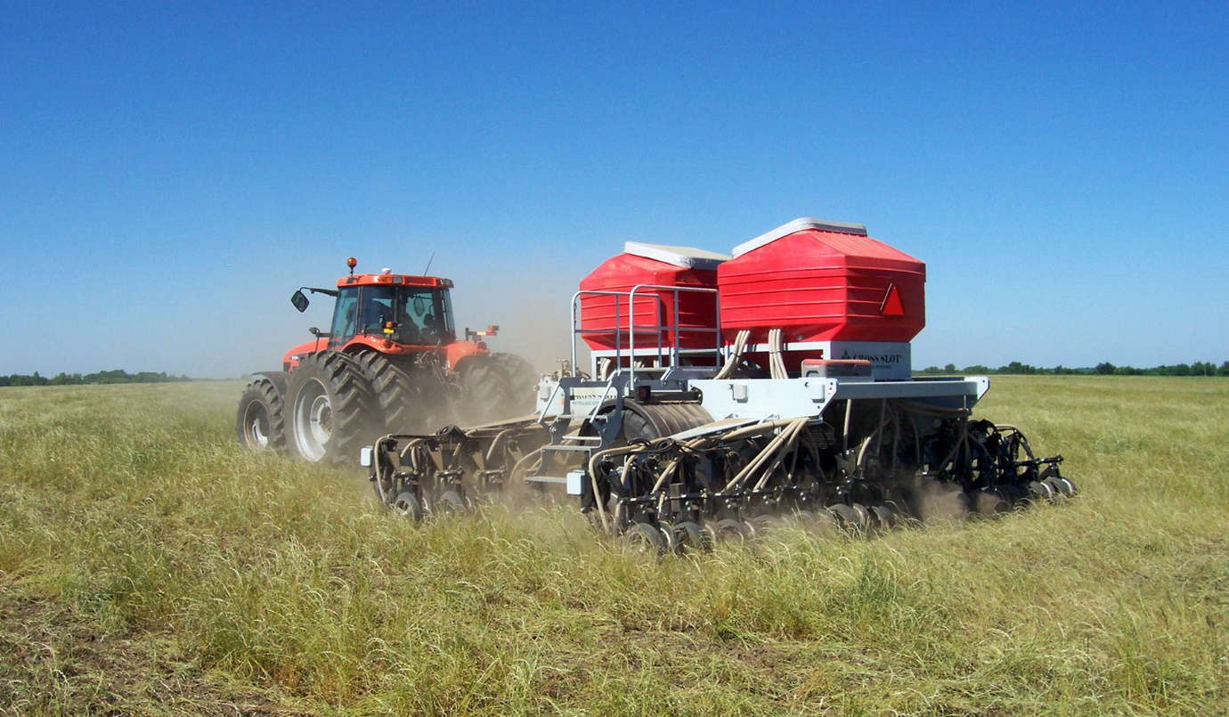 A tractor pulls a seeder though long, untilled grass.